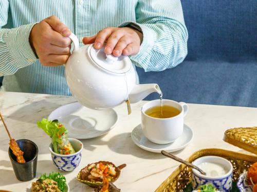a person pouring tea into a tea pot on a table at Holiday Inn Bangkok by IHG in Bangkok