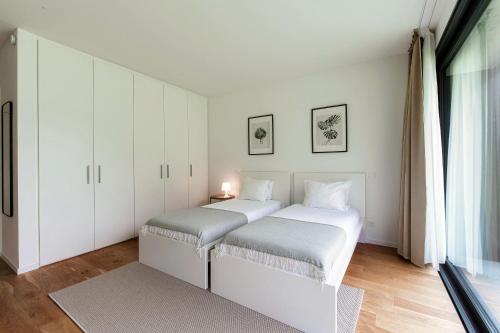 a white bedroom with two beds and a window at Residenza Ticino by Quokka 360 - Modern Oasis near Bellinzona in Bellinzona