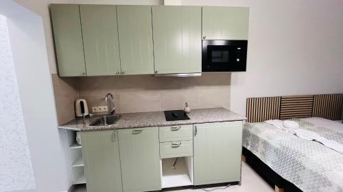 a small kitchen with green cabinets and a bed at Vitality Apartman in Makó