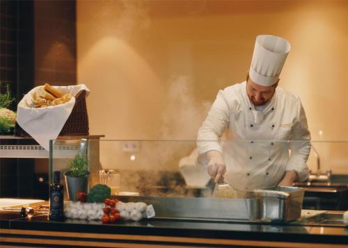 a chef standing in a kitchen preparing food at Lufthansa Seeheim - More than a Conference Hotel in Seeheim-Jugenheim