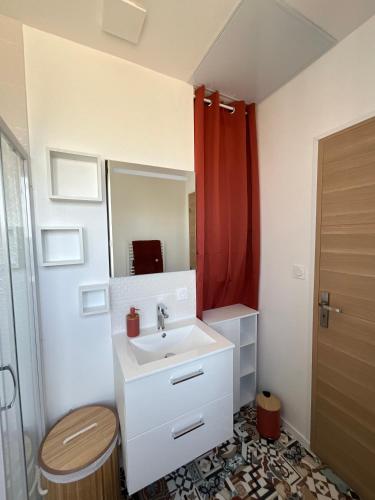 La salle de bains est pourvue d'un lavabo et d'un rideau de douche rouge. dans l'établissement Appartement à 10 minutes à pied de la mer, à Plougoulm