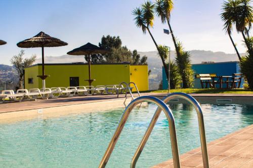 a swimming pool with chairs and umbrellas next to a building at Mobility Friends Hostel in Barcelos