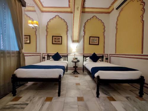 two beds in a room with yellow walls at Hotel Narain Niwas Palace in Jaipur