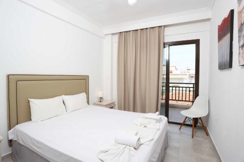 a white bedroom with a bed and a balcony at Stratos Angels apartments in Pefkohori