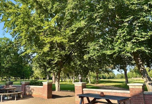 a picnic table and benches in a park with trees at Golfing & Family Breaks in Luxury Lodge in Tydd Saint Giles
