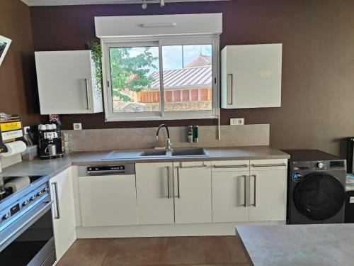 a kitchen with white cabinets and a sink and a window at Au Vendangeoir Gîte de groupe piscine in Couvignon