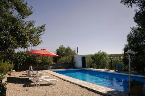 una piscina con una sombrilla roja y sillas al lado en El Brinco, en Aznalcóllar