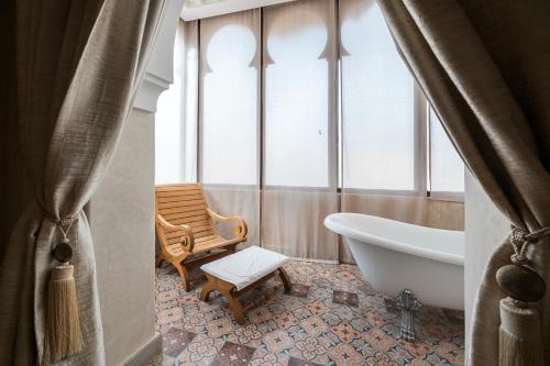 a bathroom with a tub and a chair next to a window at Pickalbatros Hôtel Du Golf - Adults Friendly 16 Years Plus- All-Inclusive in Marrakech
