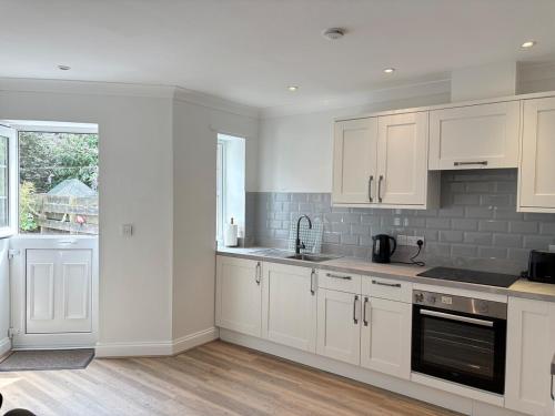 a white kitchen with white cabinets and a window at La Mouette in Mevagissey