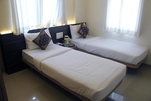 two beds in a hotel room with windows at Hotel SaiPrasad Executive Solapur in Solapur