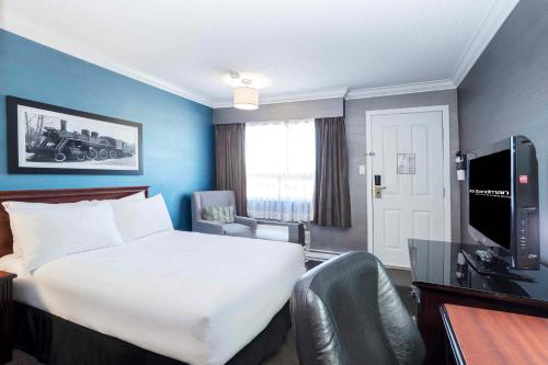 a hotel room with a bed and a desk and a television at Sandman Hotel & Suites Prince George in Prince George
