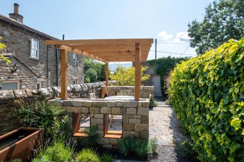 a stone walled garden with a wooden pergola at Wayside in Carperby