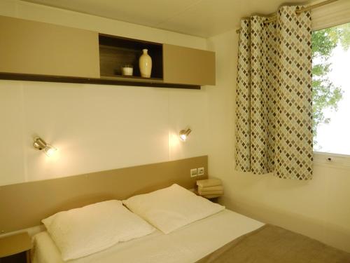 a bedroom with a bed with two pillows and a window at Mobil home 6 personnes Mer et Pins in Piriac-sur-Mer