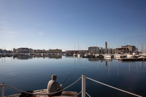 a man sitting on a dock fishing in a marina at URBANAUTS STUDIOS Ginnastica in Trieste