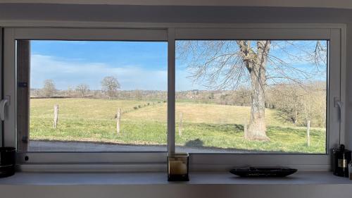 a window with a view of a field and a tree at Maison Hémera, une pause en Auvergne in Lapeyrouse