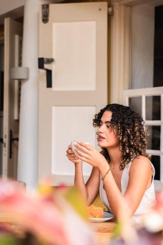 a woman sitting at a table drinking a cup of coffee at Landhuis Daniel - Plantation House in Tera Kora