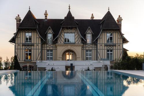 an old house with a swimming pool in front of it at Maison Douce Époque - Deauville in Bénerville-sur-Mer