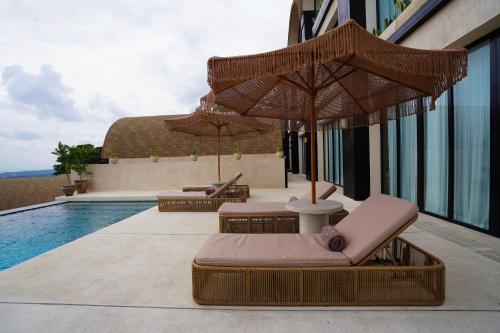two lounge chairs and umbrellas next to a swimming pool at Sunny Samudra in Uluwatu