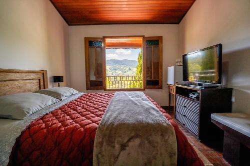 a bedroom with a bed and a television and a window at Pousada Vale do Café in Bueno Brandão