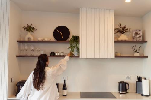 a woman is reaching for a clock on a shelf at Wahapu Lodge - Luxury sea views in Russell