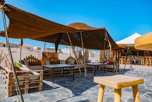 a patio with tables and chairs under a large umbrella at Agafay Yes We Camps & Spa in El Karia