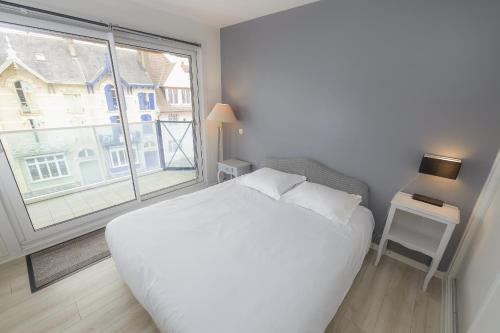 une chambre avec un lit blanc et une grande fenêtre dans l'établissement Le Grand Bleu, à Wimereux