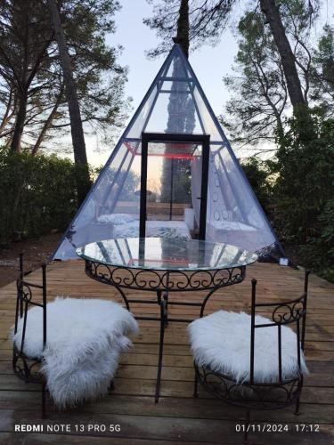 a glass table with two chairs and a tent at Logements insolites du Domaine de la Tuilière in Carnoules