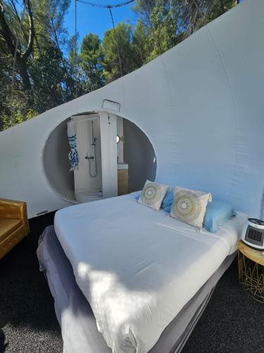 a bed in a white room with a round window at Logements insolites du Domaine de la Tuilière in Carnoules