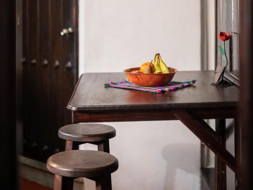 a bowl of fruit on a wooden table with two stools at Apartamentos Antigua in Antigua Guatemala