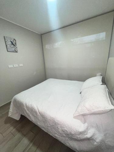 a small bedroom with a bed with white sheets and pillows at Moderno departamento a metros de Movistar Arena in Santiago