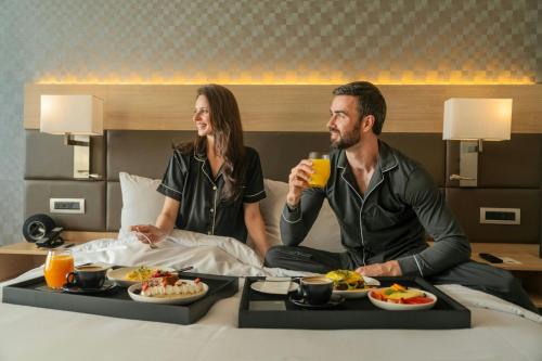 a man and woman sitting on a bed with plates of food at AC Hotel by Marriott Lima Miraflores in Lima