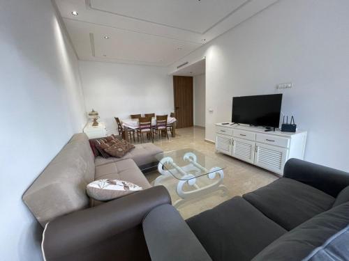 a living room with a couch and a flat screen tv at Appartement Luxe Vue Piscine Résidence Les Perles de Bentriaa, El Mansouria in Mohammedia
