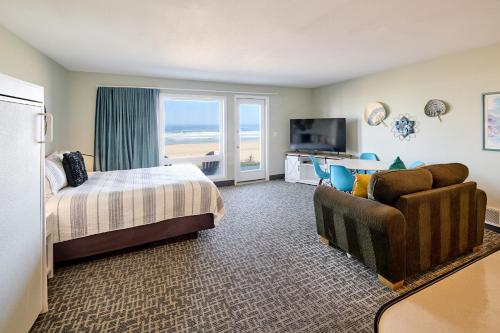 a hotel room with a bed and a couch and a television at Beachfront Condo - Ground Floor - Ocean Views - Pool & Hot Tub in Lincoln City