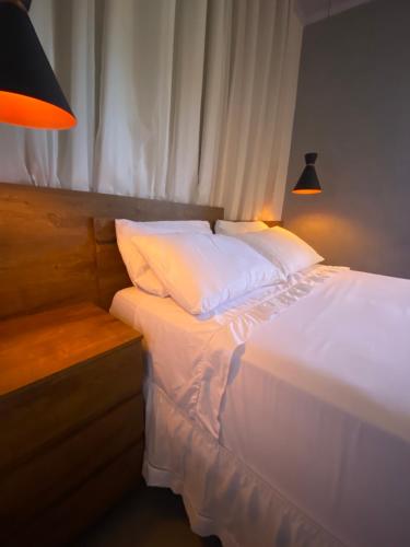 a bed with white sheets and pillows next to a window at Amoras suítes in Sao Jorge