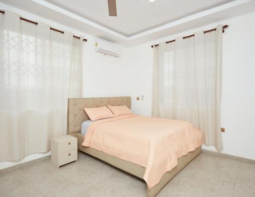 a white bedroom with a bed with pink pillows at Monroe Luxury Apartments in Kumasi