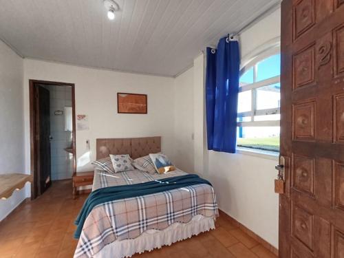 a bedroom with a bed with blue curtains and a window at Pousada e Restaurante Dona Siroba in Morretes