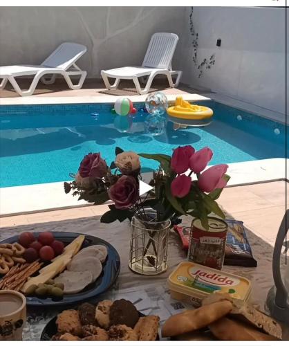 a table with food next to a swimming pool at Villa Maya House - Cap Zbib in Banī ‘Aţāʼ