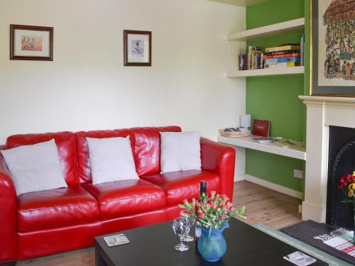 a red leather couch in a living room with a fireplace at Kinnettas Cottage in Strathpeffer