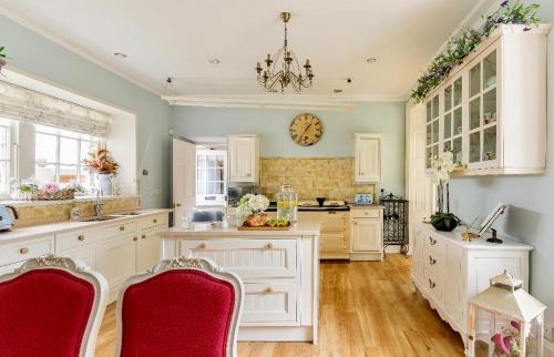 a kitchen with white cabinets and a clock on the wall at Spacious 3-Bed Manor & Jacuzzi & BBQ Cabin in Maybole
