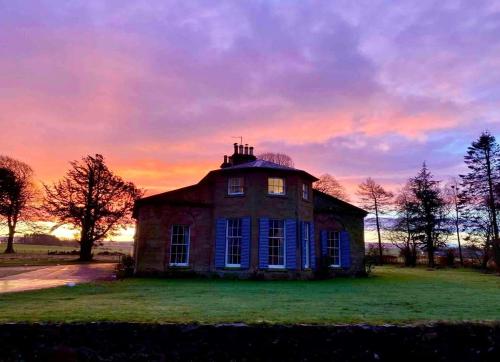 an old house on a field with a sunset in the background at Spacious 3-Bed Manor & Jacuzzi & BBQ Cabin in Maybole
