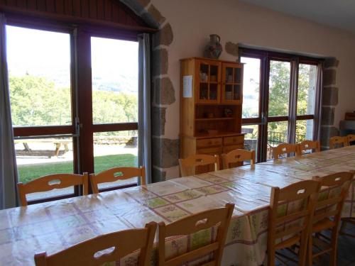 une salle à manger avec une table, des chaises et des fenêtres dans l'établissement Retraite en Montagne Bourbonnaise: Gîte Convivial pour 14 Pers., Proche Loisirs et Nature - FR-1-489-343, à La Chabanne