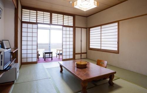 a living room with a table in a room with windows at Hotel Yakushima Sanso in Yakushima