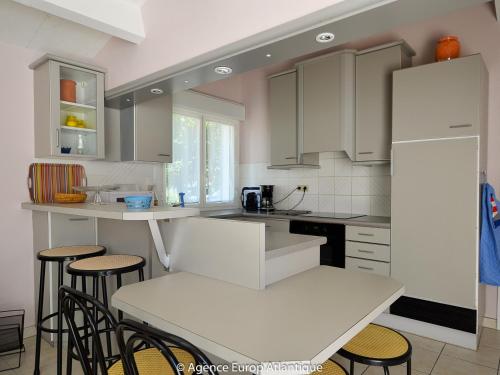 une cuisine avec des placards blancs, une table et des tabourets dans l'établissement Maison 3 chambres à La Palmyre - Près de la mer, Parking, WIFI, Animaux admis - FR-1-705-14, à La Palmyre