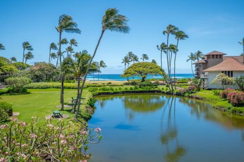 a pond with palm trees and the ocean in the background at Kiahuna Plantation Resort Kauai by OUTRIGGER in Koloa