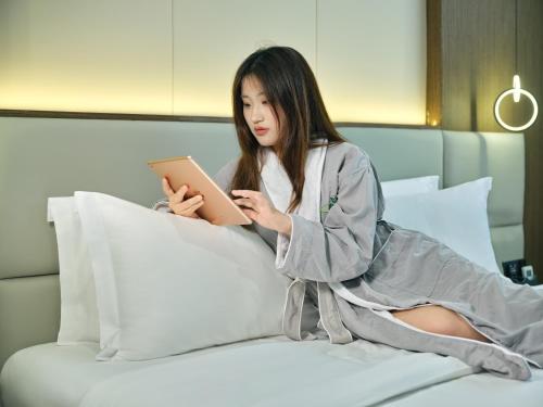 a woman sitting on a bed looking at a tablet at Lumina Boutique Hotel in Zhangjiajie
