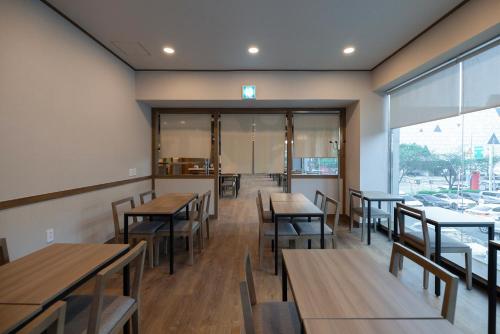 a restaurant with wooden tables and chairs and windows at Aank Ryokan Hotel Songtan in Pyeongtaek