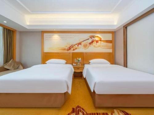 two beds in a hotel room with a painting on the wall at Vienna Hotel Guangxi Fangcheng in Fangcheng