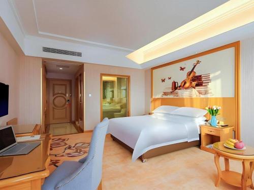 a bedroom with a bed and a desk and a computer at Vienna Hotel Taicang Shanghai East Road Landu Branch in Zhoujiating