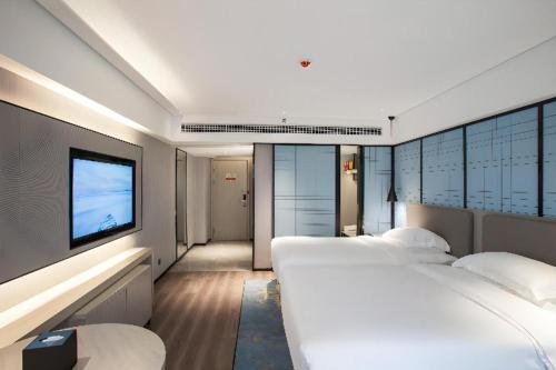 a row of white beds in a room with a tv at Echarm Hotel Leiyang in Leiyang