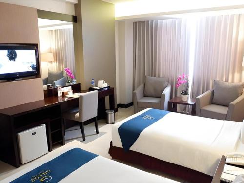 a hotel room with a bed and a desk and a television at Grage Hotel Cirebon in Cirebon